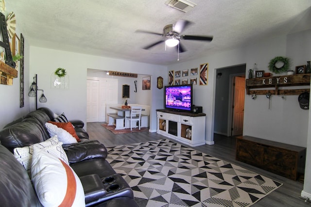 living room with a textured ceiling, ceiling fan, dark wood finished floors, and visible vents