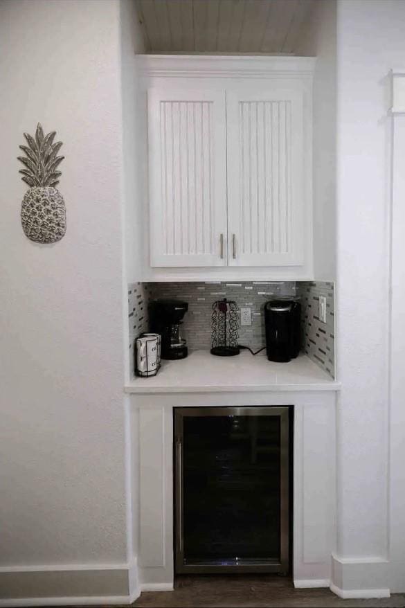 bar with tasteful backsplash, white cabinets, and beverage cooler