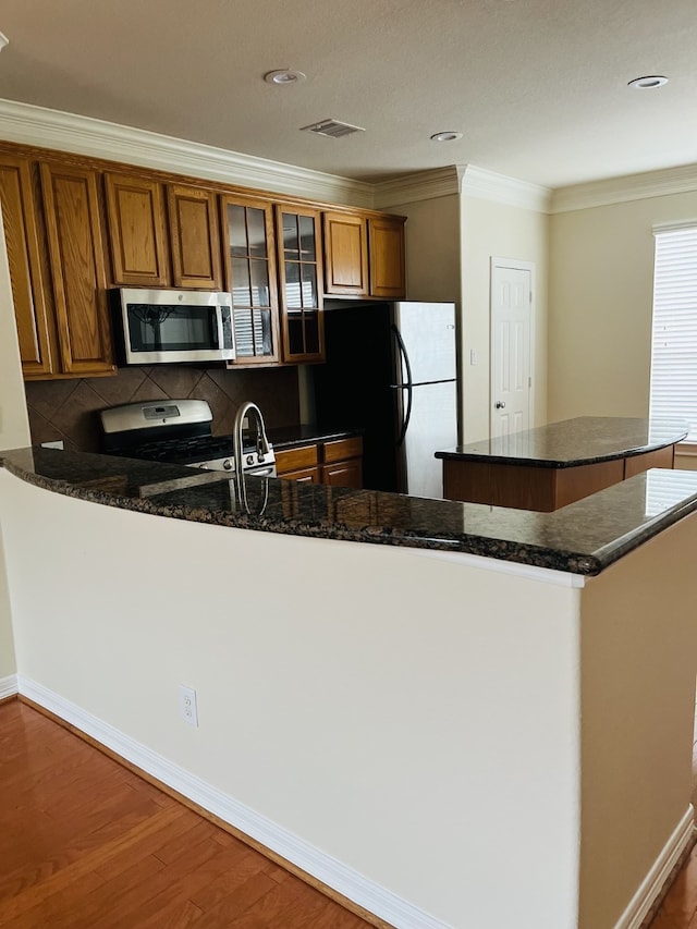 kitchen with backsplash, crown molding, dark stone counters, appliances with stainless steel finishes, and hardwood / wood-style flooring