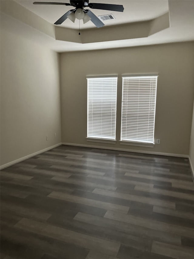 empty room featuring dark hardwood / wood-style flooring, a tray ceiling, and ceiling fan