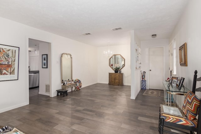 hall with a textured ceiling, dark wood-type flooring, and a chandelier