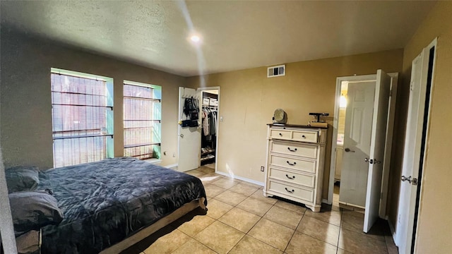 bedroom featuring a walk in closet, light tile patterned floors, a textured ceiling, and a closet