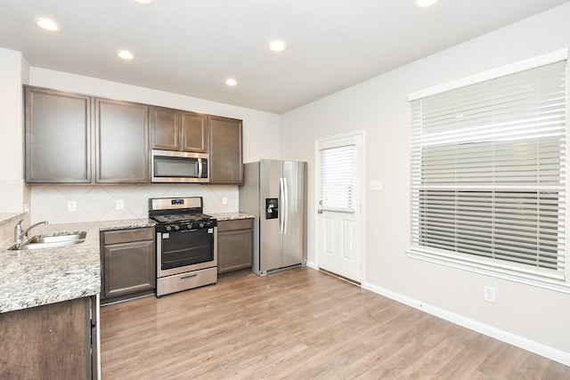 kitchen with light stone countertops, appliances with stainless steel finishes, tasteful backsplash, sink, and light hardwood / wood-style floors