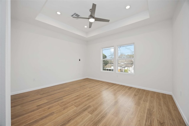 empty room featuring light wood-type flooring, ceiling fan, and a raised ceiling