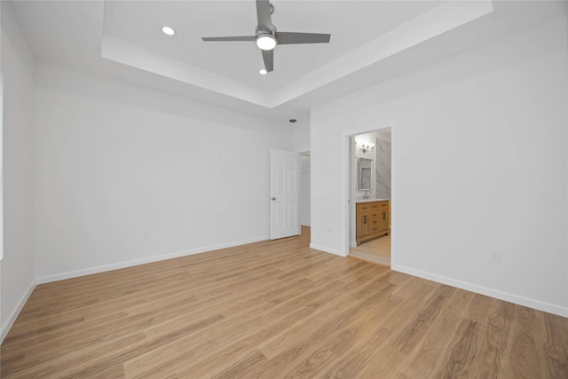 unfurnished bedroom with a raised ceiling, light wood-type flooring, ensuite bathroom, and ceiling fan