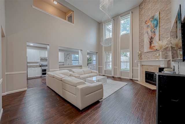 living room with an inviting chandelier, dark hardwood / wood-style flooring, a towering ceiling, and a tiled fireplace