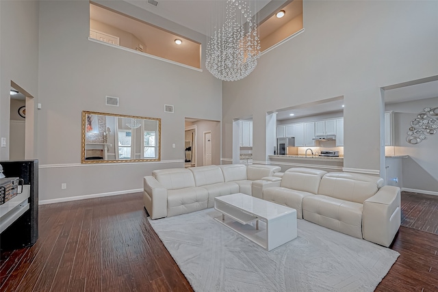 living room featuring sink, a high ceiling, an inviting chandelier, hardwood / wood-style floors, and a fireplace