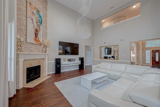 living room with a tile fireplace, a high ceiling, an inviting chandelier, and dark wood-type flooring