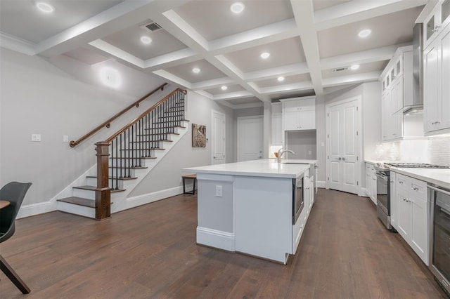 kitchen with white cabinets, backsplash, a kitchen island with sink, and stainless steel gas range