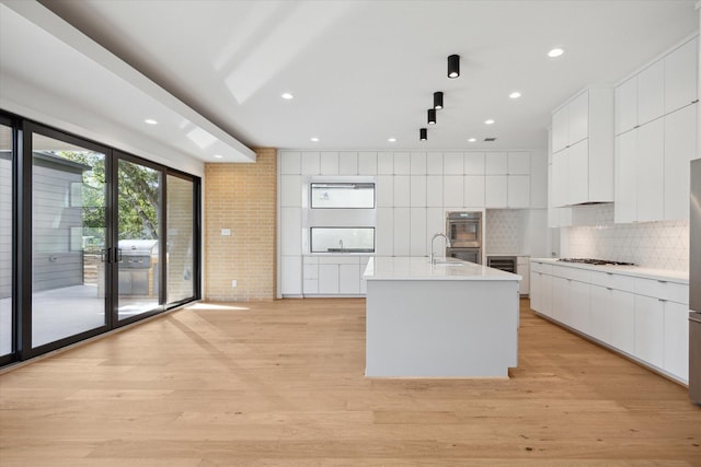 kitchen with tasteful backsplash, an island with sink, white cabinetry, and light hardwood / wood-style floors