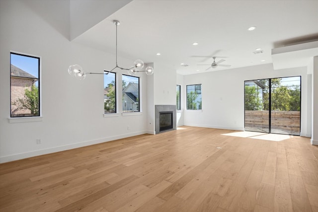 unfurnished living room featuring a fireplace, ceiling fan with notable chandelier, and light hardwood / wood-style flooring