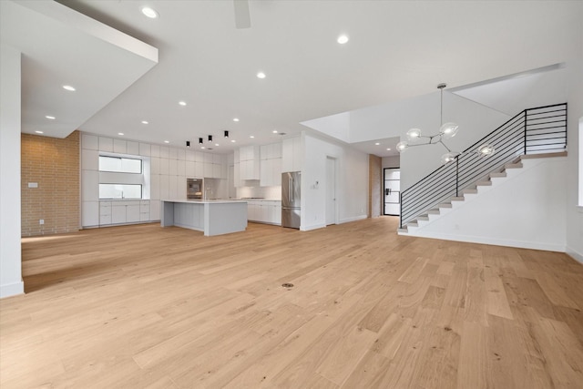 unfurnished living room featuring brick wall, a chandelier, and light hardwood / wood-style floors