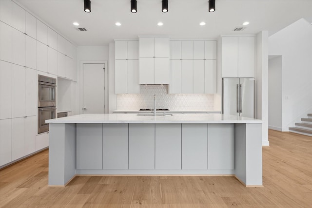 kitchen with a large island with sink, white cabinets, backsplash, and stainless steel appliances