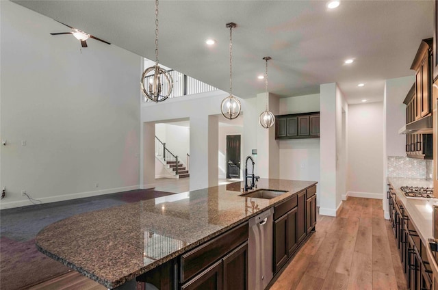 kitchen featuring dark brown cabinetry, a large island, sink, stainless steel dishwasher, and dark stone countertops