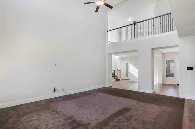 unfurnished living room with ceiling fan, carpet floors, and a high ceiling