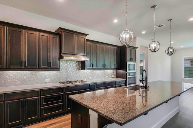 kitchen featuring light stone counters, sink, an island with sink, and appliances with stainless steel finishes