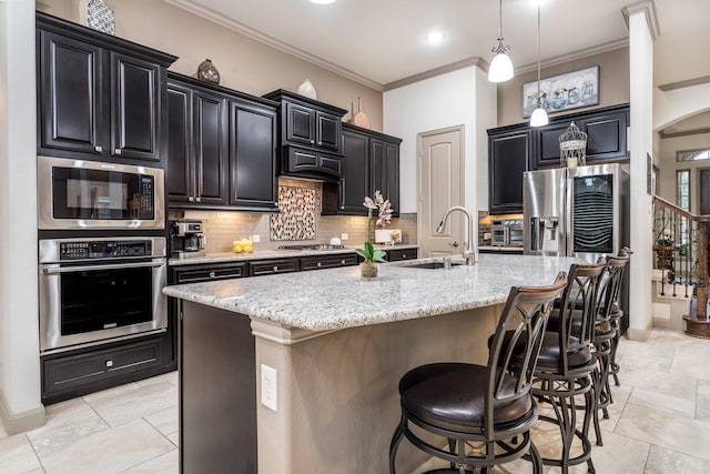 kitchen with a kitchen bar, stainless steel appliances, a kitchen island with sink, decorative light fixtures, and sink