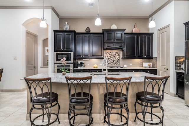 kitchen with light stone countertops, stainless steel appliances, an island with sink, sink, and backsplash