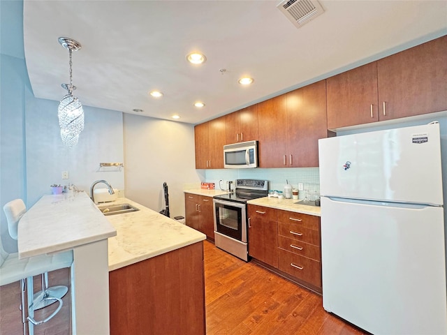 kitchen with kitchen peninsula, appliances with stainless steel finishes, sink, hanging light fixtures, and a breakfast bar area