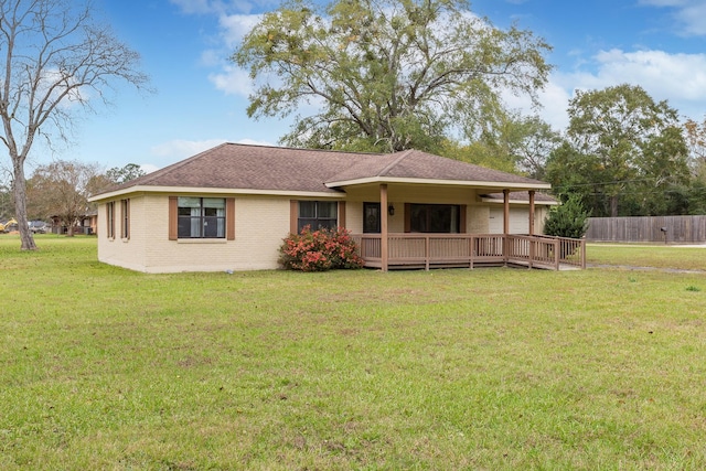 view of front of property with a deck, brick siding, fence, roof with shingles, and a front yard