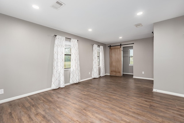 unfurnished room featuring dark wood-style floors, a barn door, visible vents, and baseboards