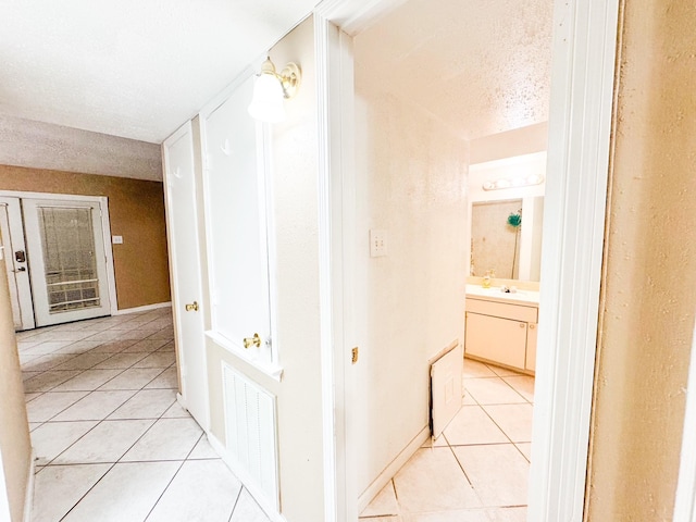 corridor featuring light tile patterned flooring, sink, and a textured ceiling