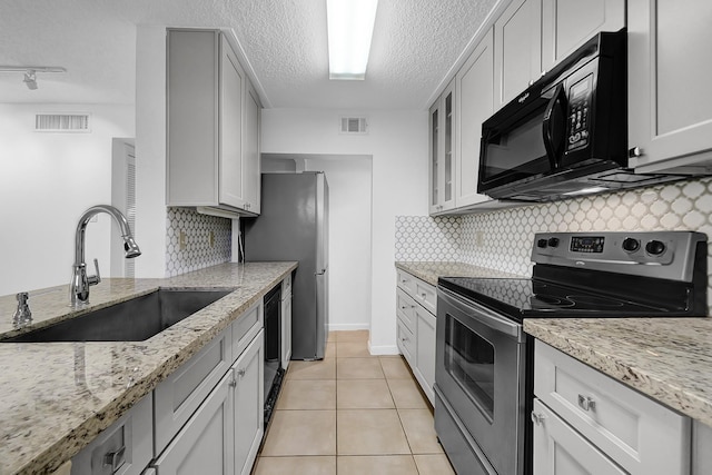 kitchen featuring black appliances, sink, rail lighting, light stone countertops, and light tile patterned floors