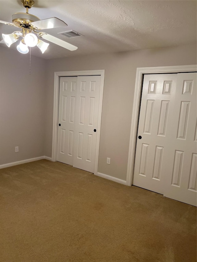 unfurnished bedroom with ceiling fan, a textured ceiling, light carpet, and two closets