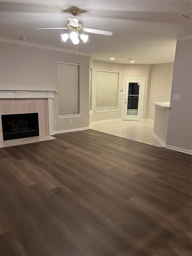 unfurnished living room with ceiling fan, crown molding, dark wood-type flooring, and a tile fireplace