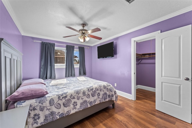 bedroom featuring ceiling fan, crown molding, a spacious closet, dark hardwood / wood-style floors, and a closet