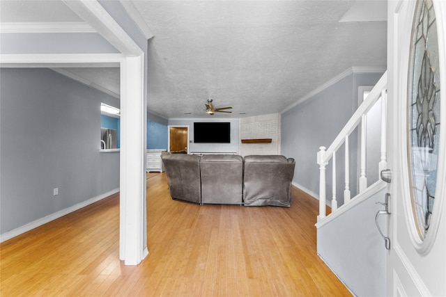 living room featuring ceiling fan, crown molding, light wood-type flooring, and a textured ceiling