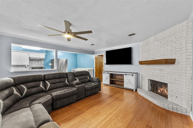 living room with light wood-type flooring, a textured ceiling, a brick fireplace, and ornamental molding