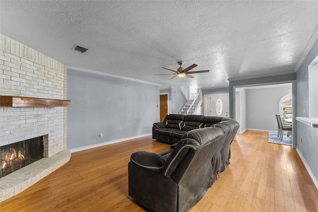 living room with a brick fireplace, a textured ceiling, ceiling fan, crown molding, and light hardwood / wood-style flooring