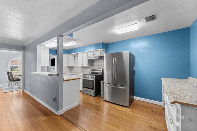 kitchen with white cabinets, light hardwood / wood-style flooring, a textured ceiling, tasteful backsplash, and stainless steel appliances