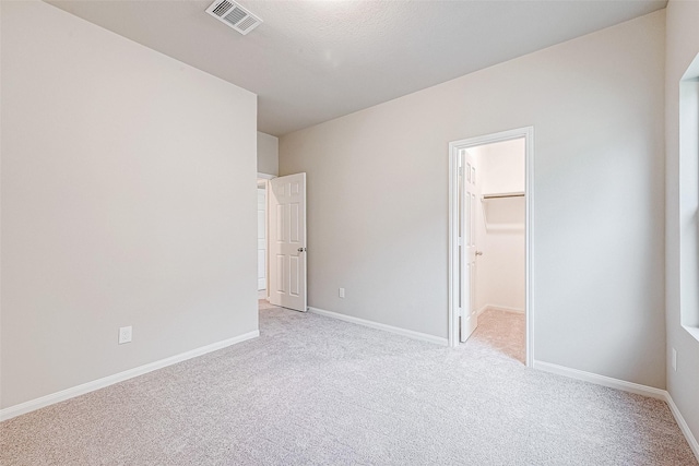 unfurnished bedroom with a closet, a spacious closet, and light carpet