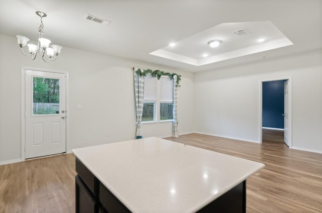 kitchen featuring a notable chandelier, a tray ceiling, light hardwood / wood-style floors, and pendant lighting