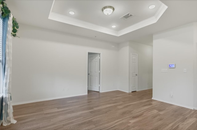 empty room with hardwood / wood-style floors, crown molding, and a raised ceiling