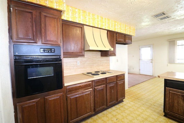 kitchen with tasteful backsplash, oven, white cooktop, a textured ceiling, and custom exhaust hood