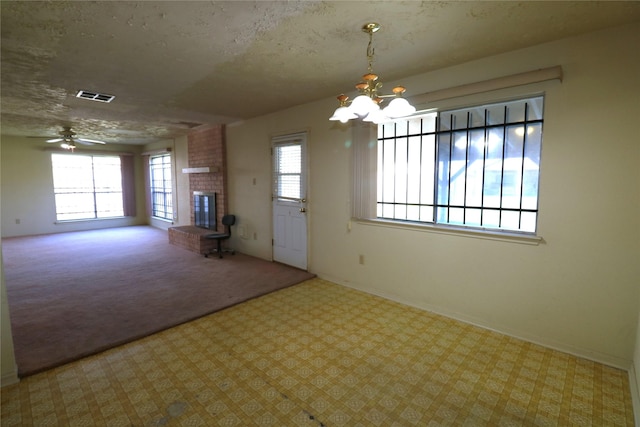 carpeted empty room with a fireplace, a textured ceiling, ceiling fan with notable chandelier, and a wealth of natural light