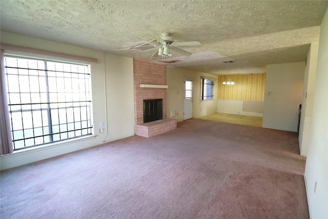 unfurnished living room with a textured ceiling, carpet floors, ceiling fan with notable chandelier, and a brick fireplace