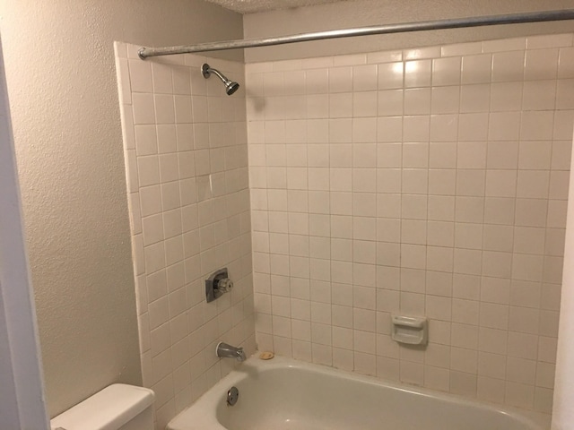 bathroom featuring toilet, a textured ceiling, and tiled shower / bath