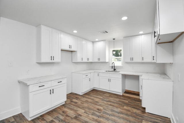 kitchen featuring pendant lighting, dark wood-type flooring, sink, light stone countertops, and white cabinetry