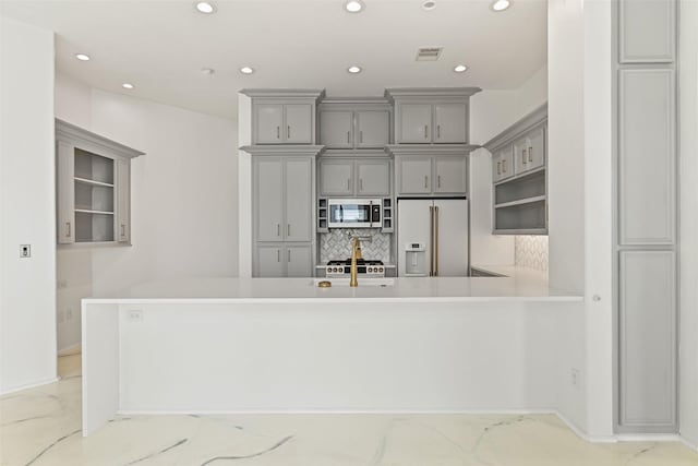 kitchen with high end fridge, gray cabinets, light countertops, stainless steel microwave, and a peninsula