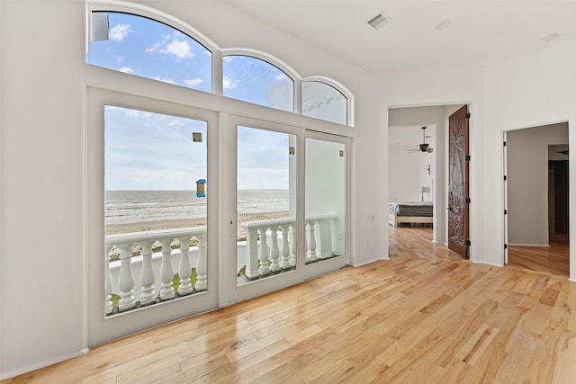 unfurnished room featuring a wealth of natural light, a water view, a beach view, and light wood finished floors