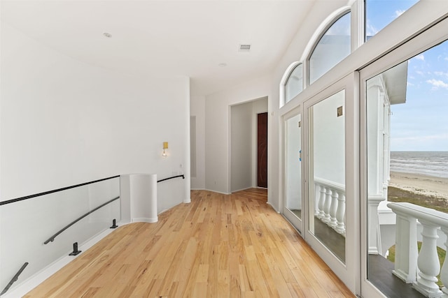 hall with light wood-style floors, a healthy amount of sunlight, a water view, and a beach view