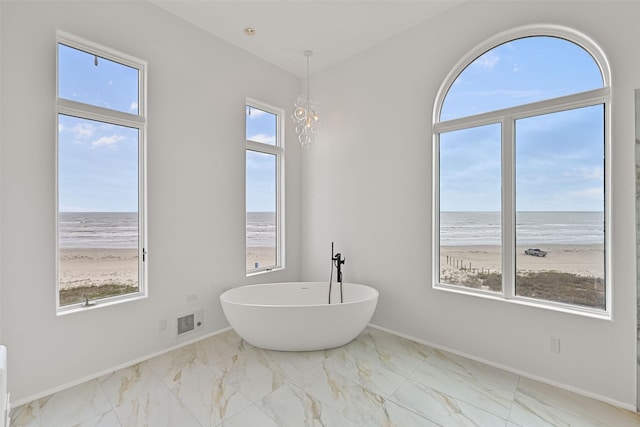 full bath featuring a water view, marble finish floor, a freestanding bath, and a view of the beach