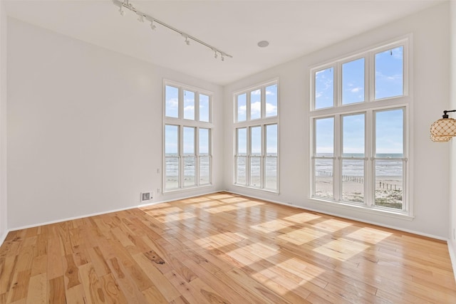 spare room featuring baseboards, a water view, a towering ceiling, and light wood-style floors