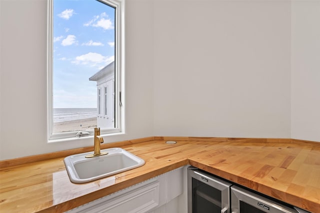 kitchen featuring a water view, butcher block countertops, white cabinetry, and a sink