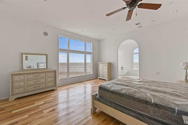 bedroom featuring light wood finished floors, visible vents, arched walkways, a ceiling fan, and ensuite bath