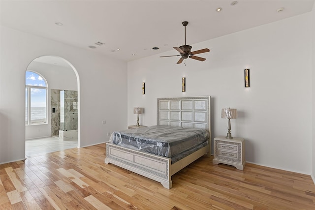 bedroom featuring arched walkways, light wood finished floors, ensuite bathroom, and recessed lighting